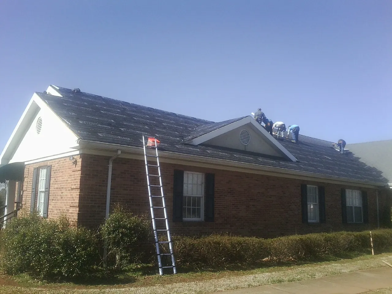 Crew tearing shingles off a brick ranch roof with a ladder set — Metal Roof Repair work by our crew in Vonore
