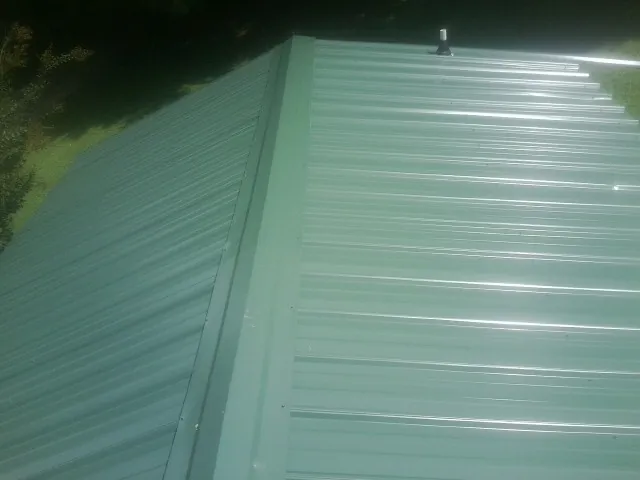 New green metal panels meeting at the ridge of a roof — Flat Roof Repair work by our crew in Vonore