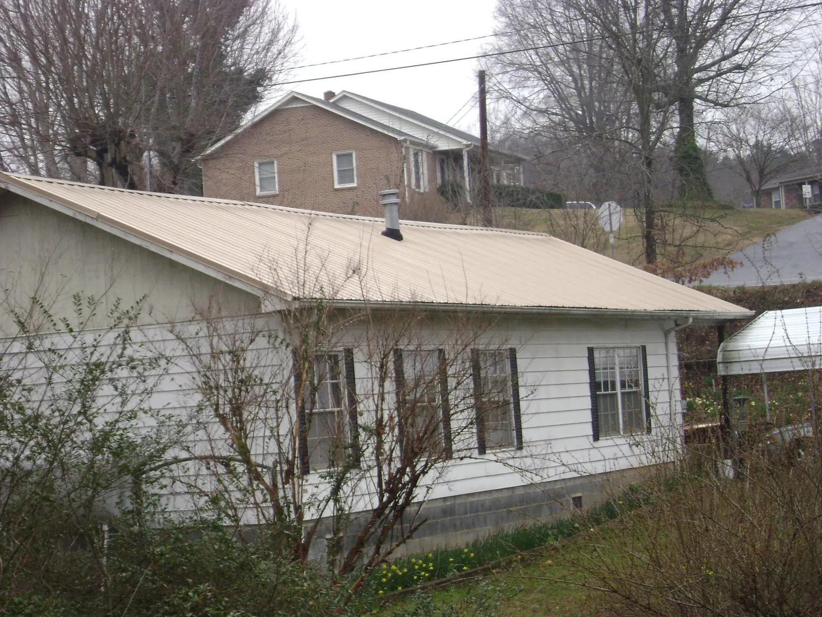 Tan metal roof on a white sided house set into a hillside — Commercial Roofing by Roofing Brothers in Vonore